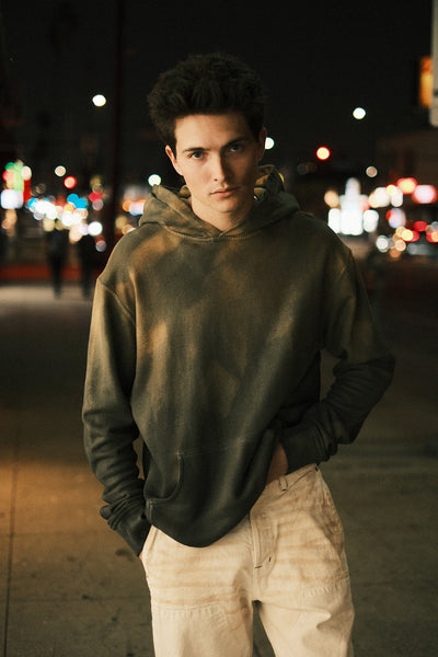 Model wearing the oil-stained hoodie with cream trousers on a city street at night