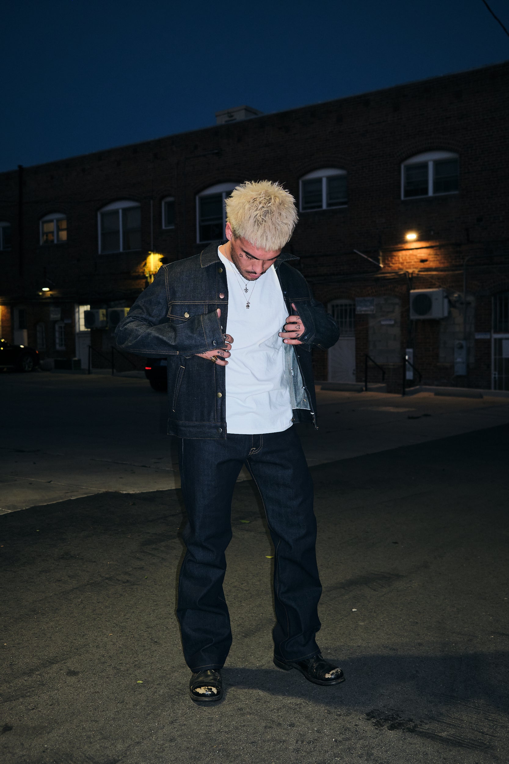 A Man Standing Out In The Open Wearing Rope indigo raw denim trucker jacket with rope indigo denim jeans with chest flap pockets and mixed metal buttons, front view