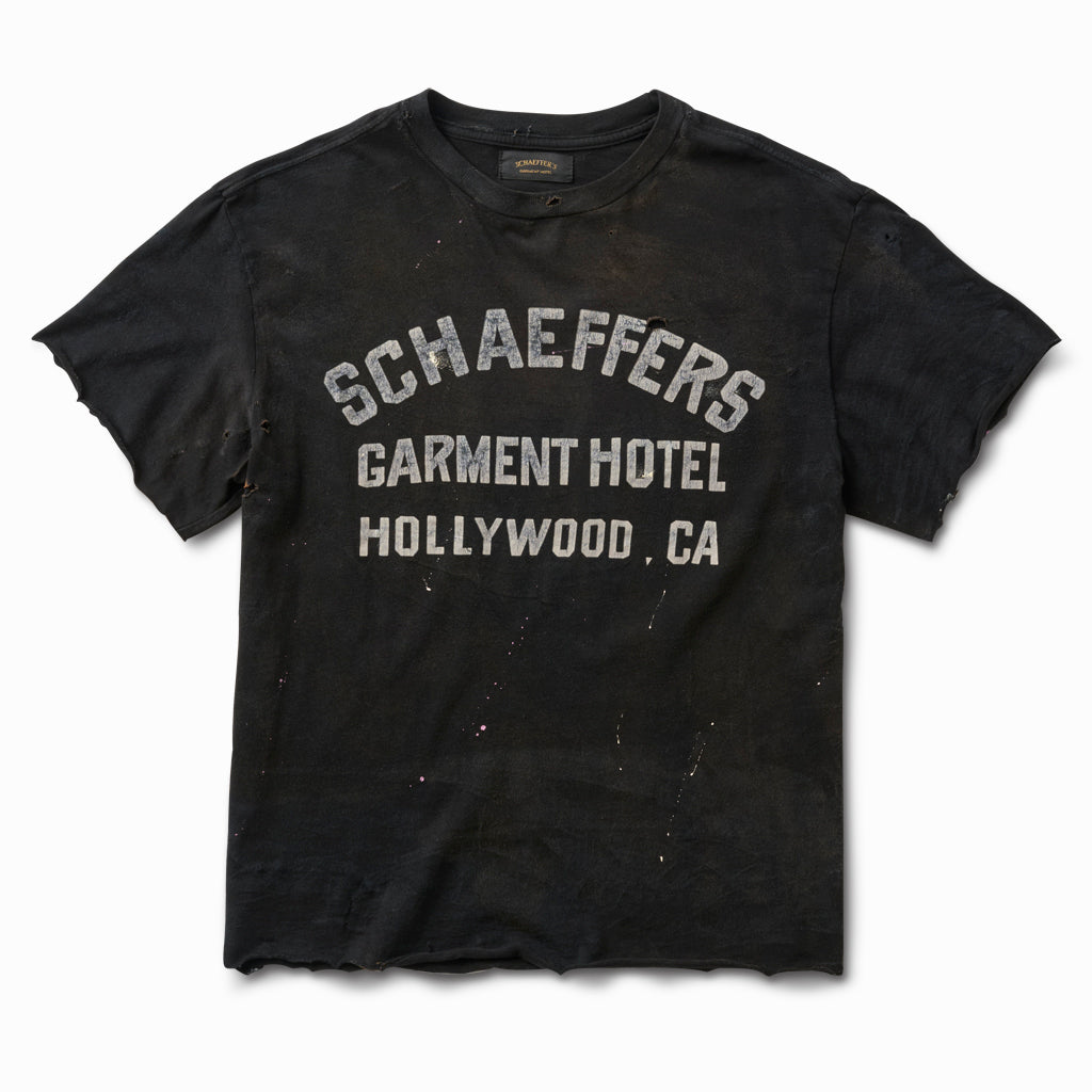 Distressed black raw cut tee with a faded white Schaeffers Garment Hotel Hollywood, CA varsity print, front view