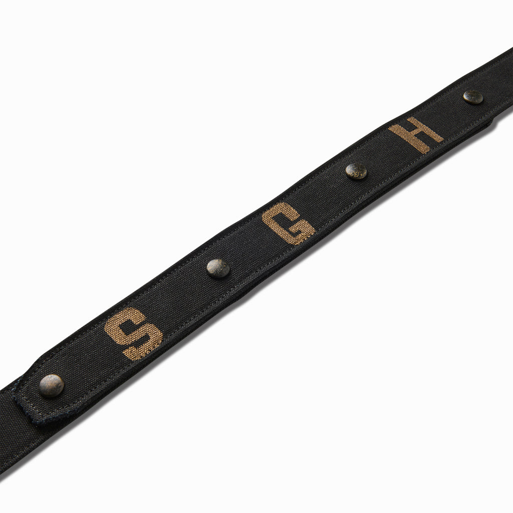 Close-up of the hand-painted tan S, G and H letters between studs on the black canvas belt