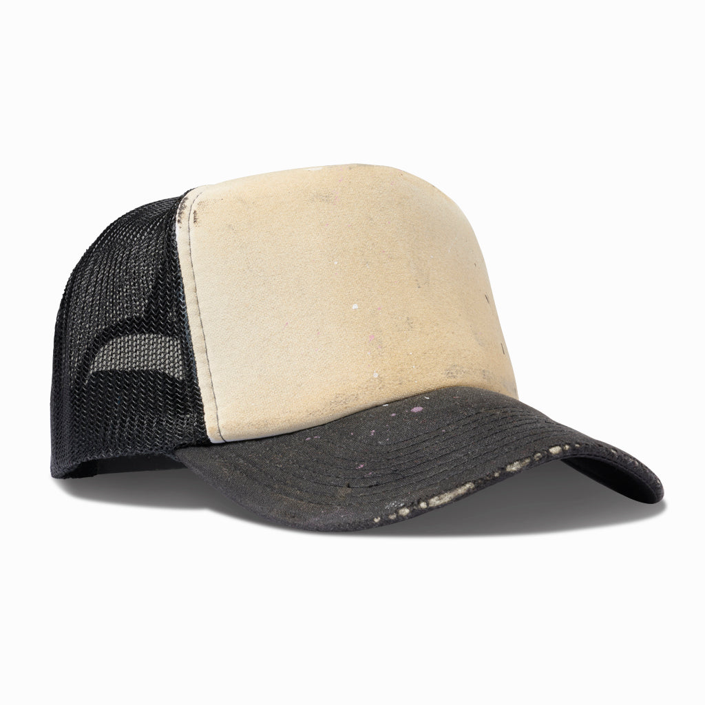 Dirty ivory and black trucker hat, angled view showing the mesh back and frayed brim