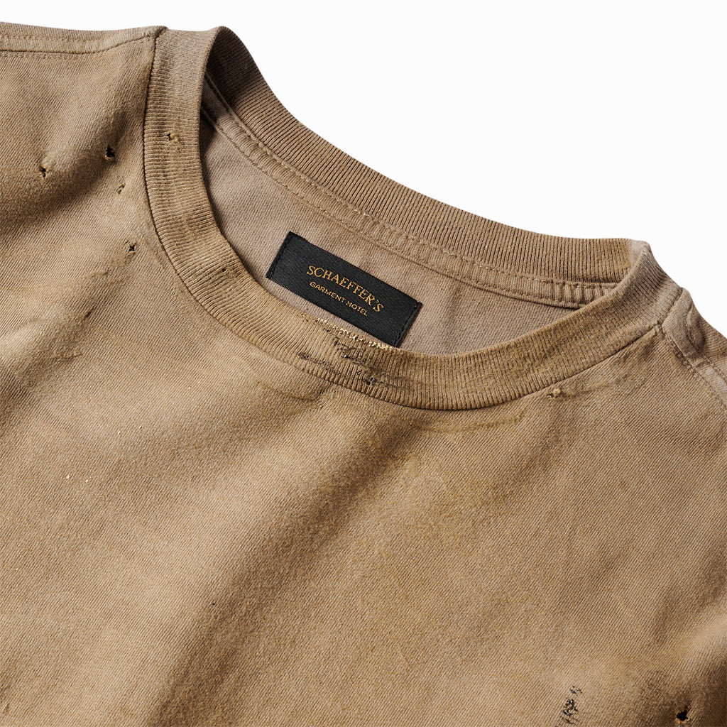 Close-up of the tan tee's ribbed collar with pinhole distressing and Schaeffer's neck label