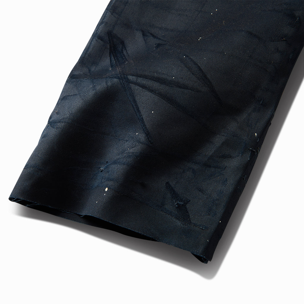 Close-up of the waxed blue chino's raw hem with paint splatter and crackled wax