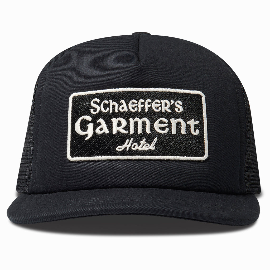 Black trucker hat with a cream Schaeffer's Garment Hotel patch, front view