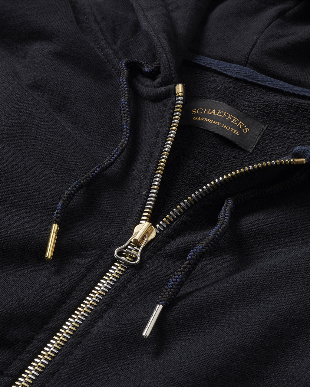 Close-up of the zip hoodie's brass zipper, drawcords with brass tips and Schaeffer's label