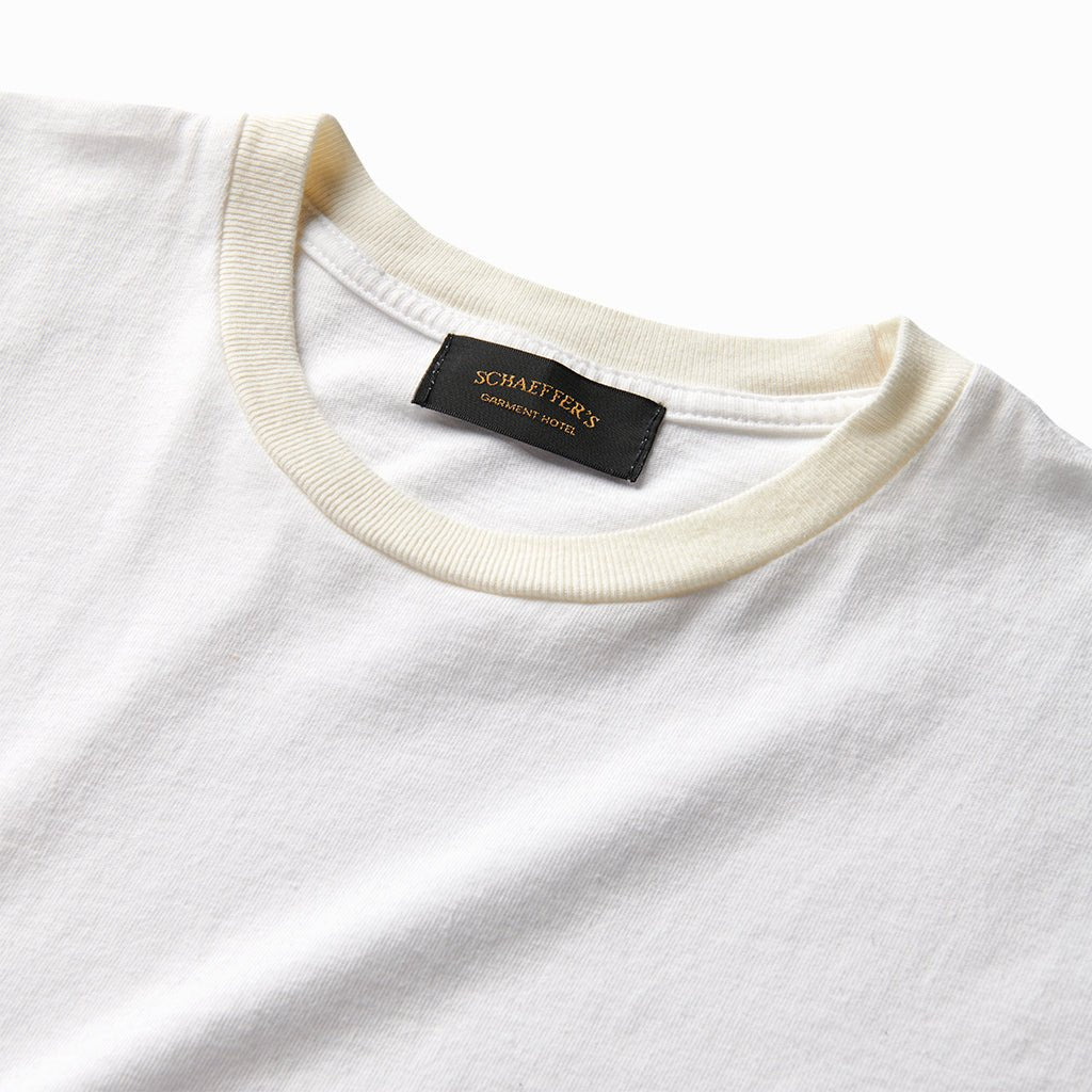 Close-up of the white athletic tee's cream ribbed collar and Schaeffer's neck label