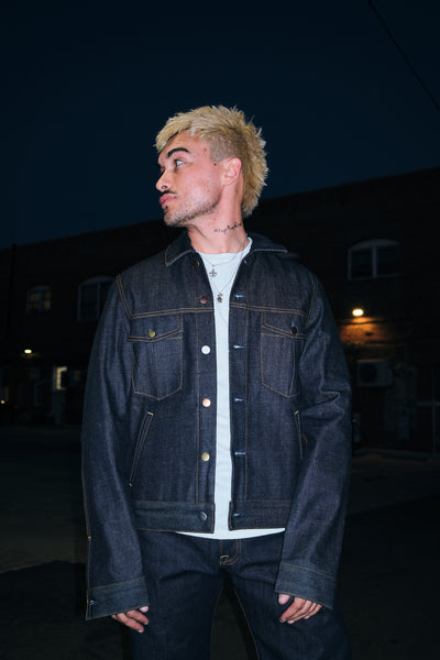 A Man Close Up Wearing Rope indigo raw denim trucker jacket with chest flap pockets and mixed metal buttons, front view