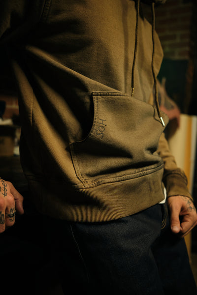 A close-up lifestyle shot of a person wearing a dark olive brown hooded hoodie.